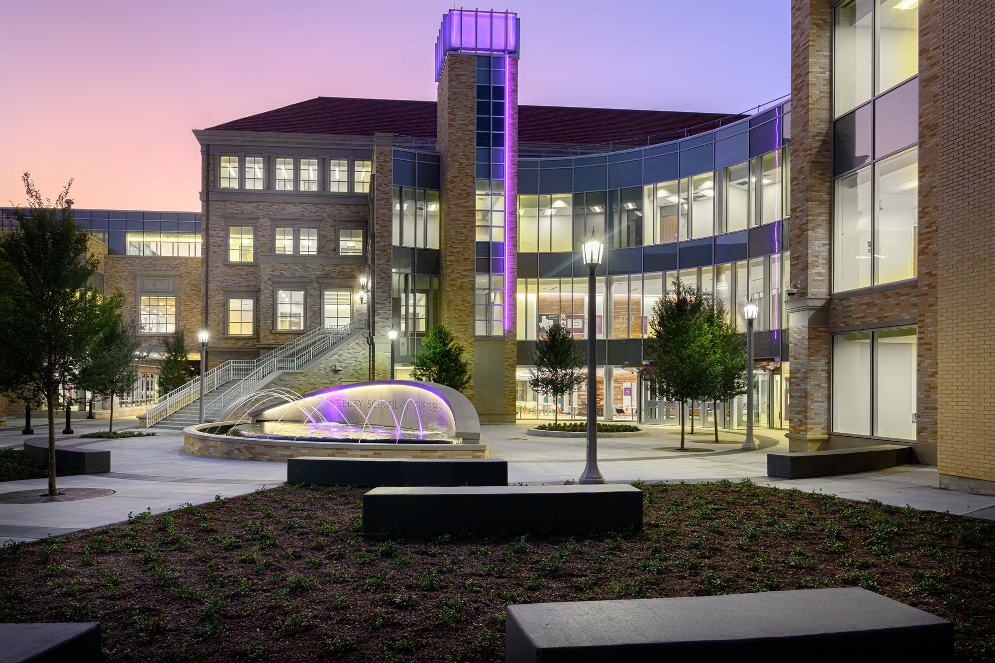 The Neeley School of Business courtyard at dusk, with the tower and fountain lit in purple