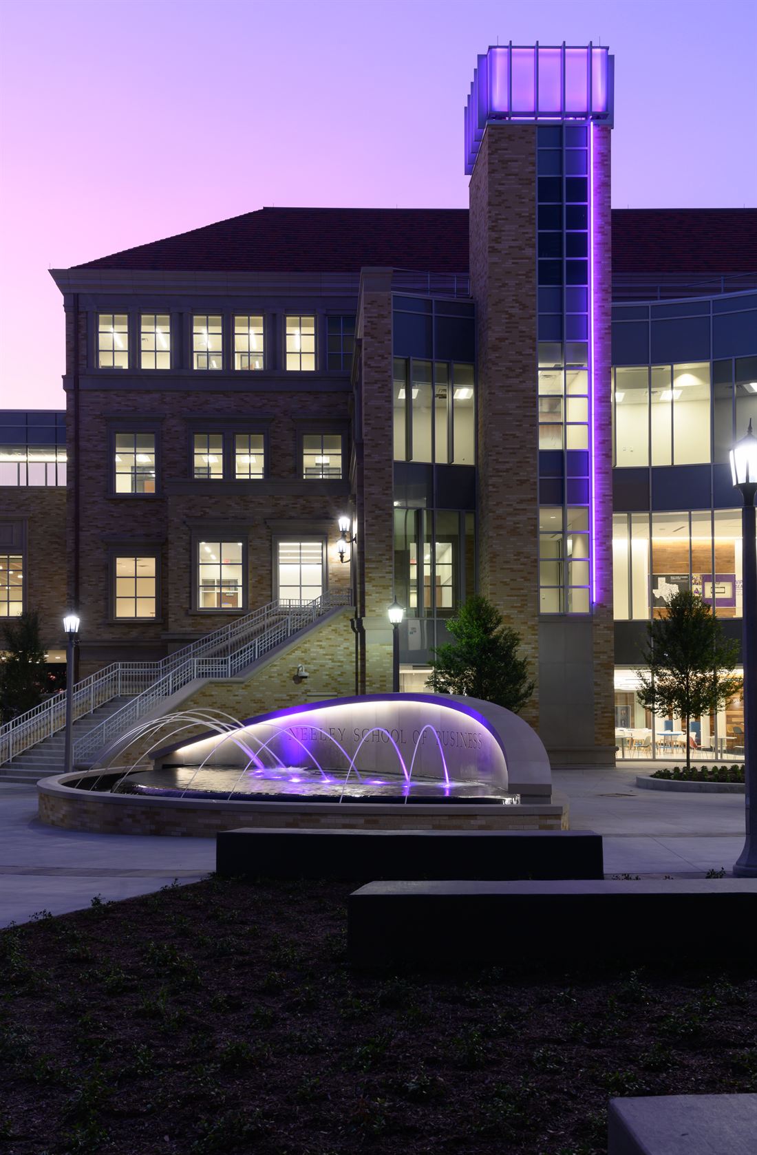 The Neeley School of Business at dusk with its purple-lit tower and fountain